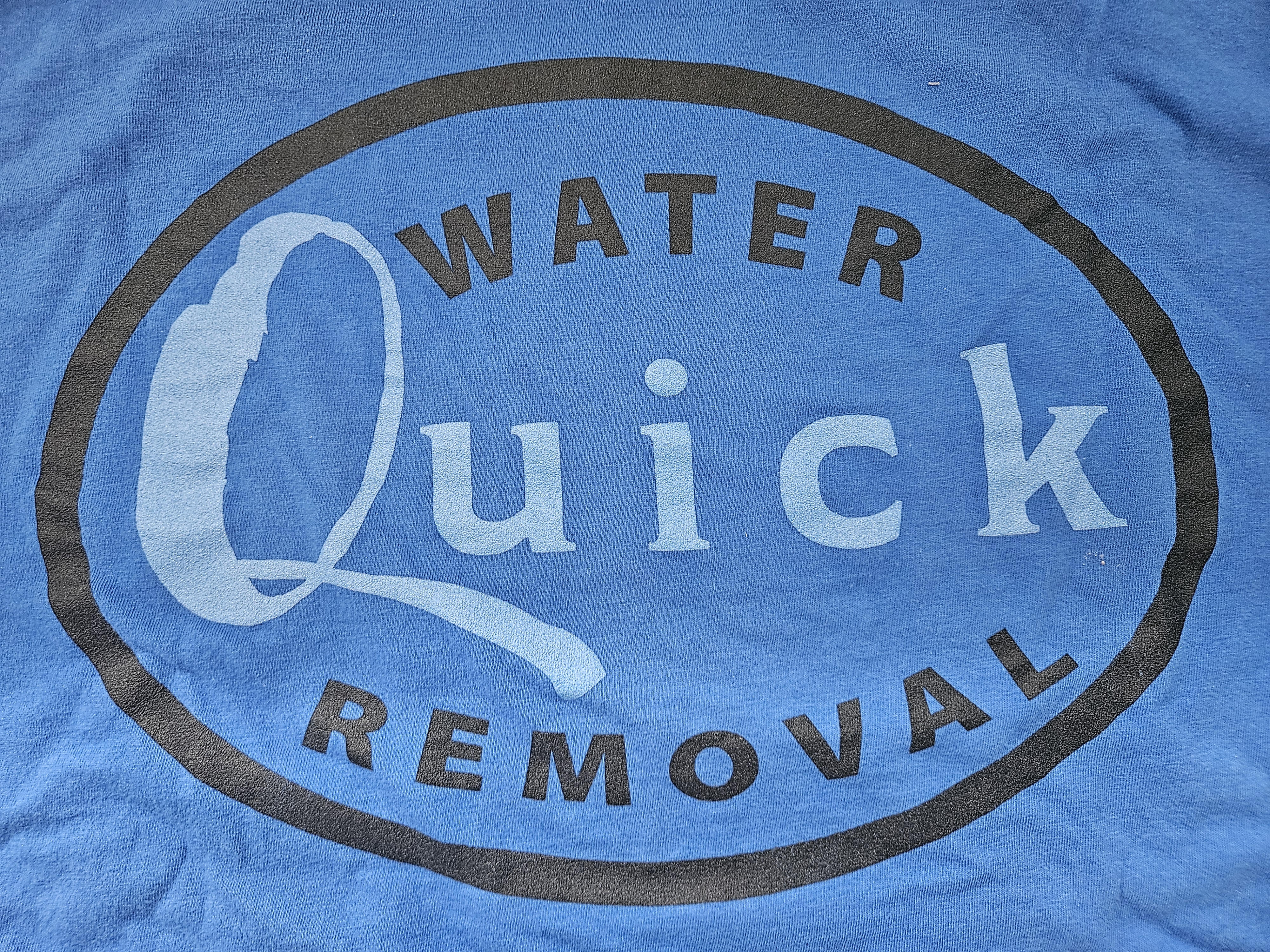 Close-up of a blue t-shirt with a water damage removal logo.